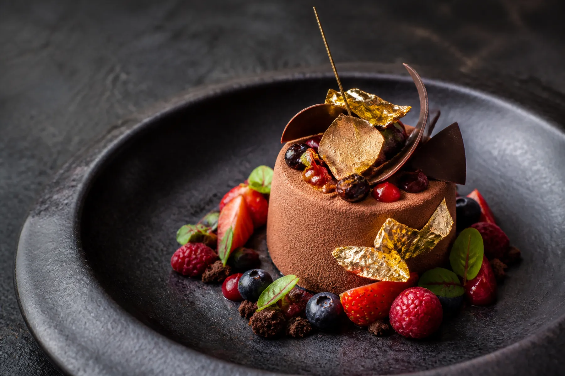 Gourmet chocolate dessert with berries and gold leaf